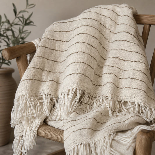 Heidi 100% cotton throw blanket with natural ivory stripes, woven texture and fringe draped over a wooden chair.