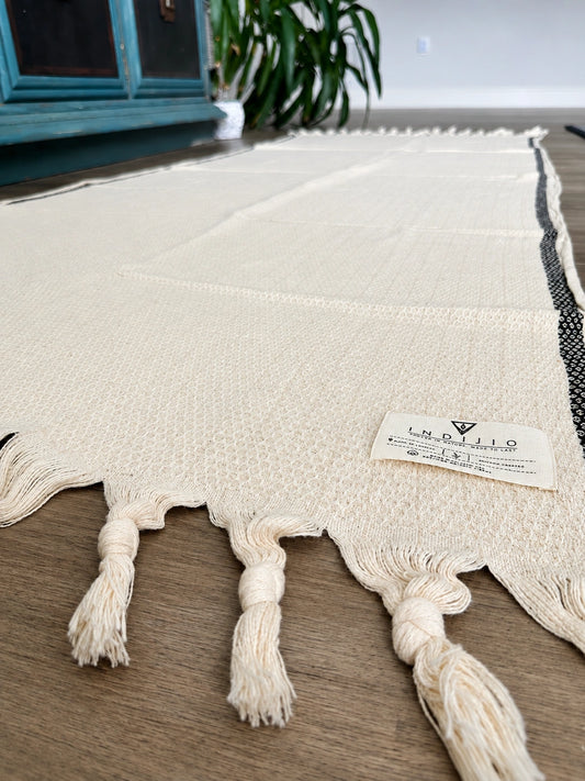 Bella 100% cotton Turkish towel in natural ivory with black woven border stripes, textured weave, knotted tassels and Indijio label.