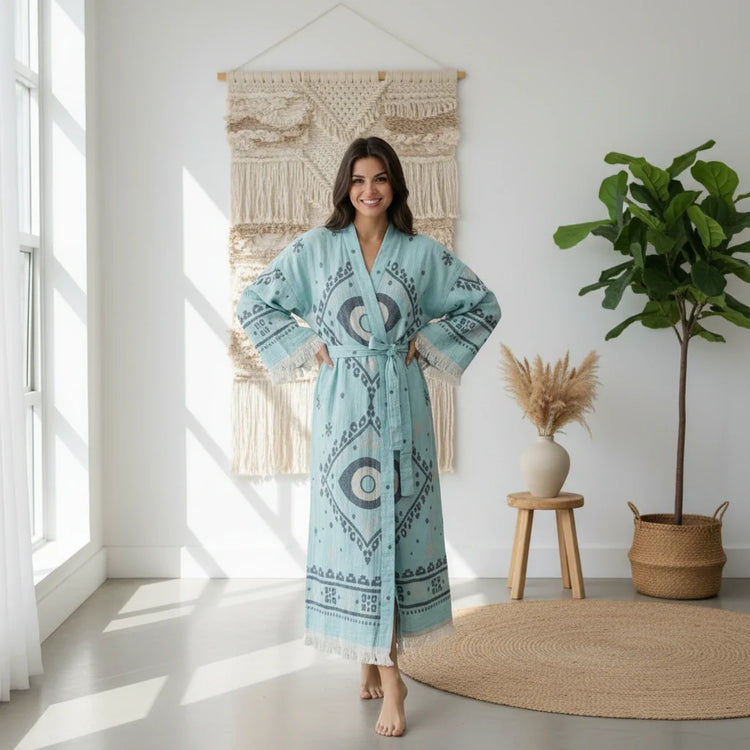 Woman wearing the Nara Green Turkish cotton kimono robe, seated in a wooden chair with a relaxed lifestyle setting.