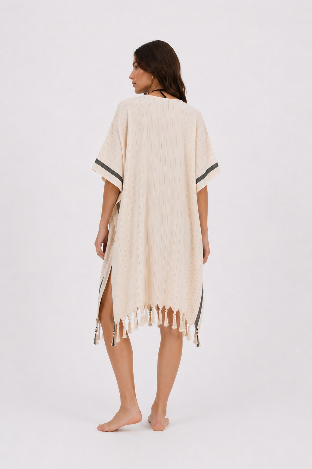A woman shown from the back wearing a cream-colored, short-sleeved cotton cover-up dress with fringe trim and dark gray sleeve stripes, set against a plain white studio background.