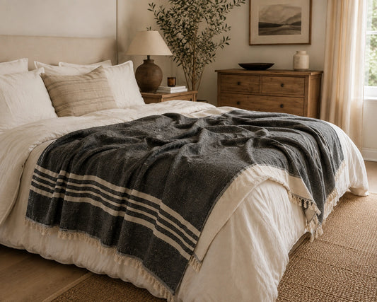 Ela black and natural striped linen cotton throw blanket layered across a neutral bed with fringed edges.