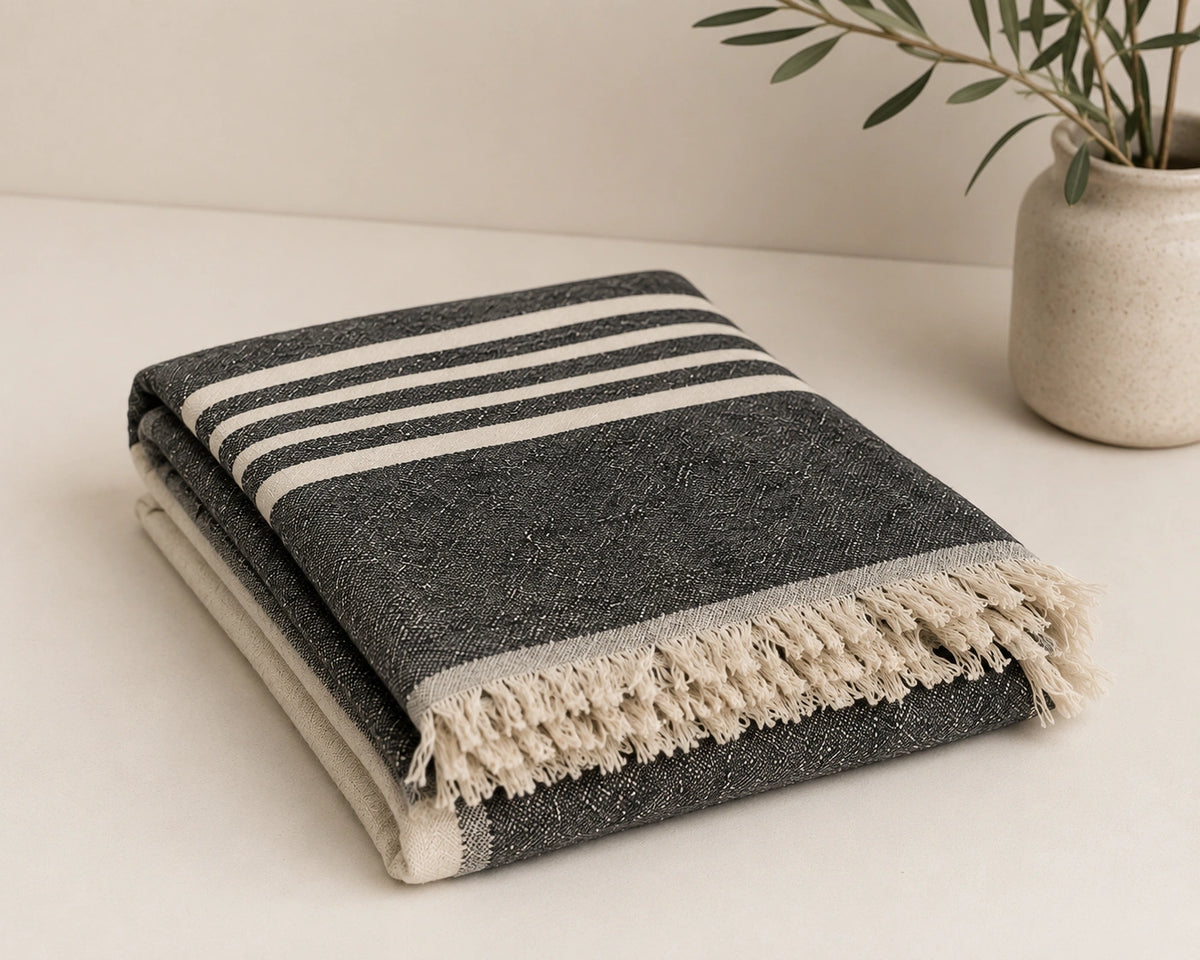Folded Ela linen cotton throw blanket in charcoal black and natural with woven stripe pattern and cream fringe.