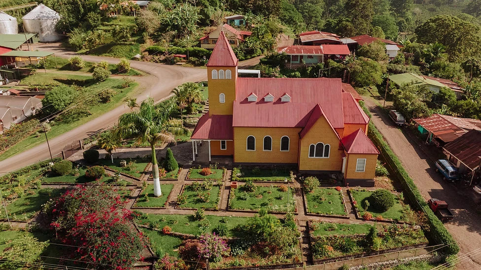 Aerial view of the historic church, gardens and lush landscape at Aquiares coffee farm in Costa Rica, surrounded by tropical greenery.