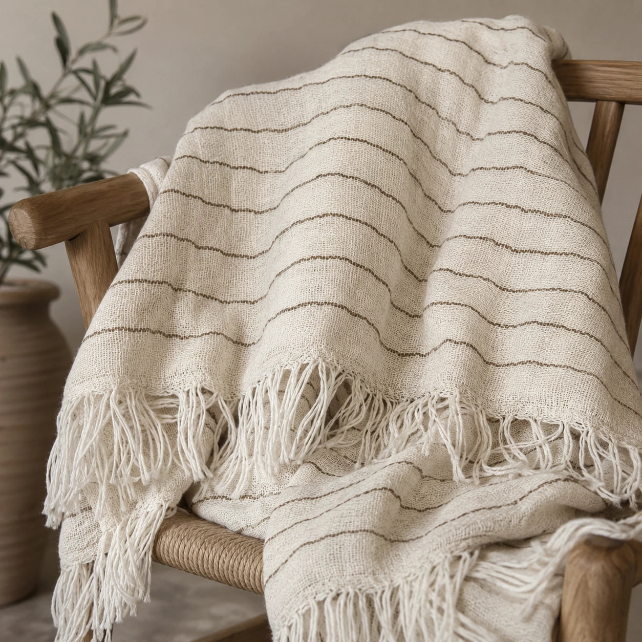 Heidi 100% cotton throw blanket with natural ivory stripes, woven texture and fringe draped over a wooden chair.