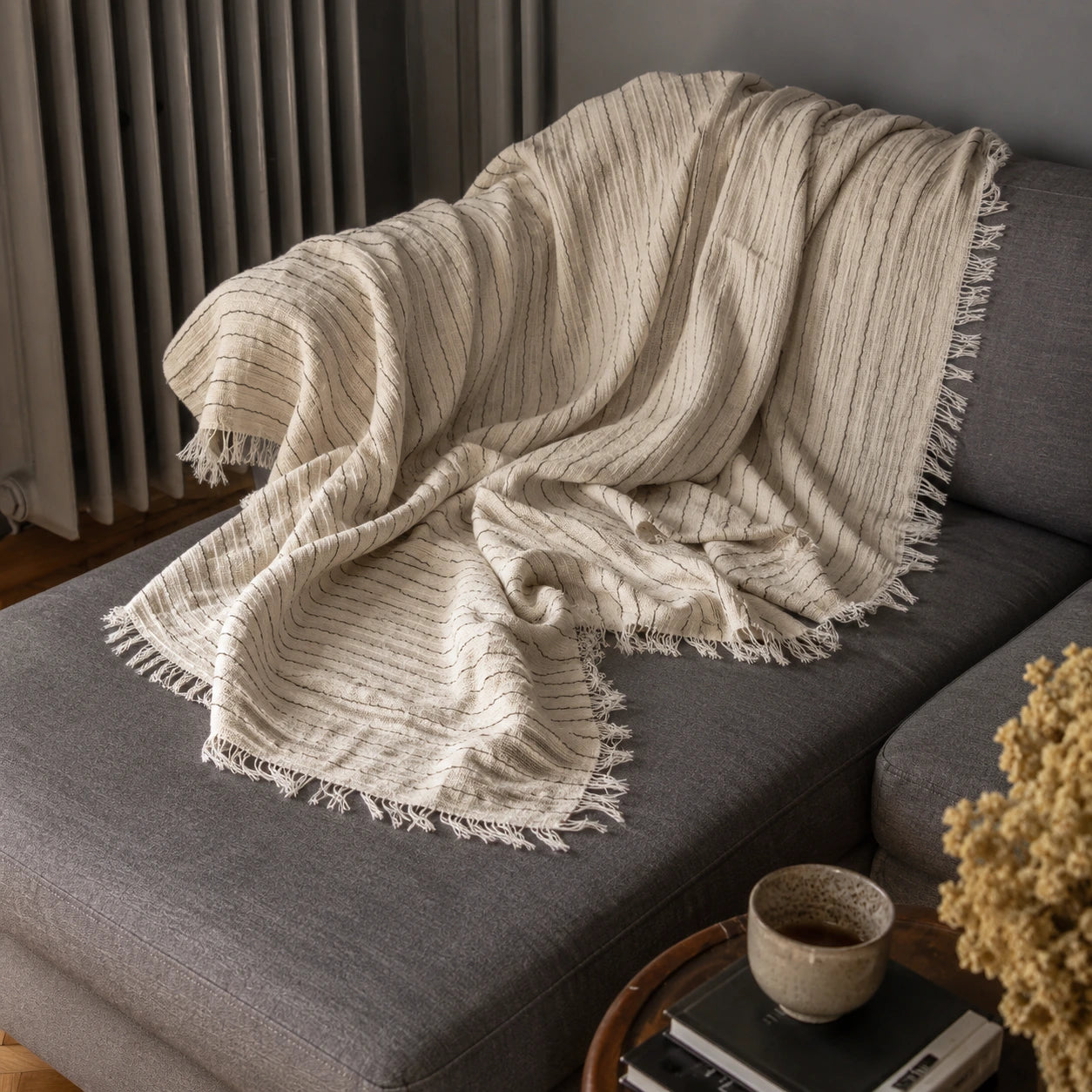 Natural ivory Heidi cotton throw blanket layered on a gray sofa, showing its soft woven texture, neutral stripes and fringe.