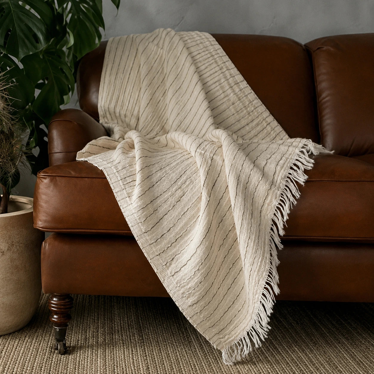 Heidi 100% cotton striped throw blanket casually draped over a brown leather sofa with natural fringed edges.