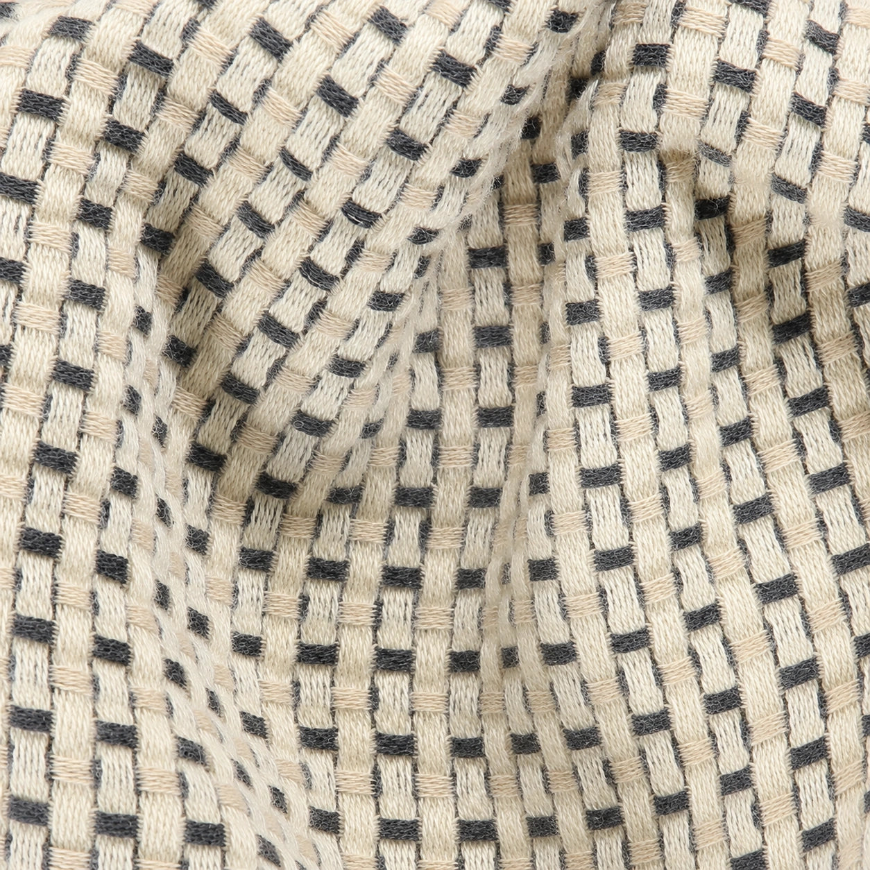 Close-up of Maya cotton throw blanket showing the dimensional cream and charcoal woven texture and natural cotton fibers.