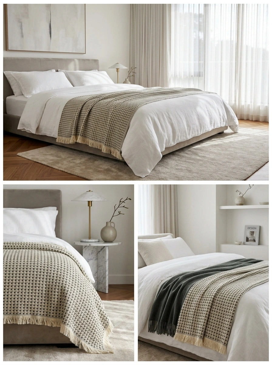 Maya cream and charcoal cotton throw blanket styled across a white bed, showing its neutral woven pattern and fringed edges.