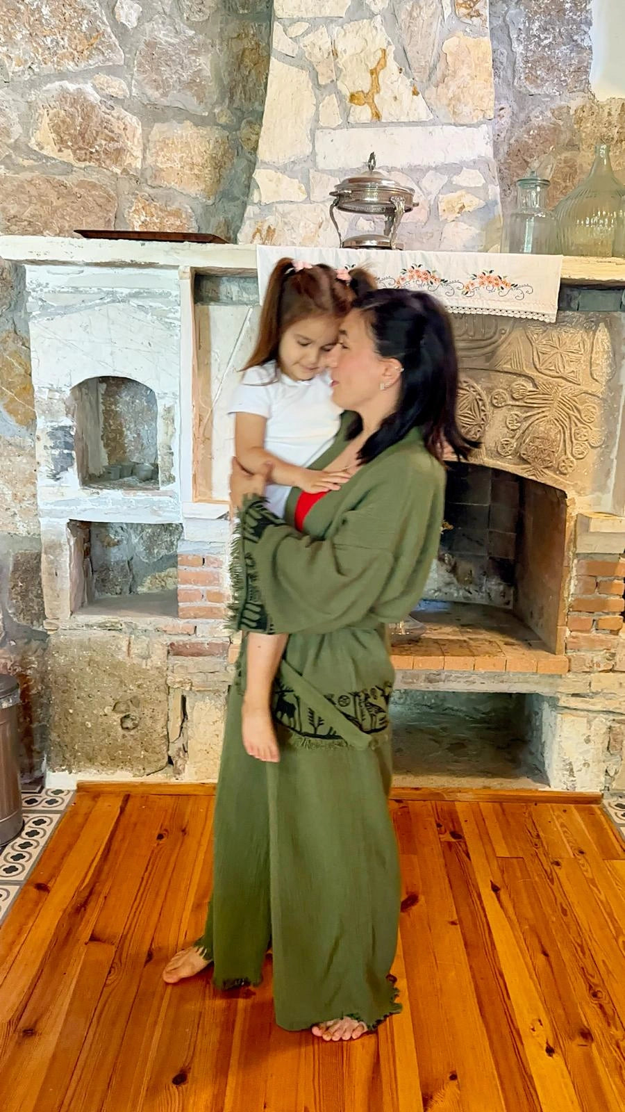 A woman in Nara kimono set holds a young girl in a rustic stone fireplace room with wooden floors.