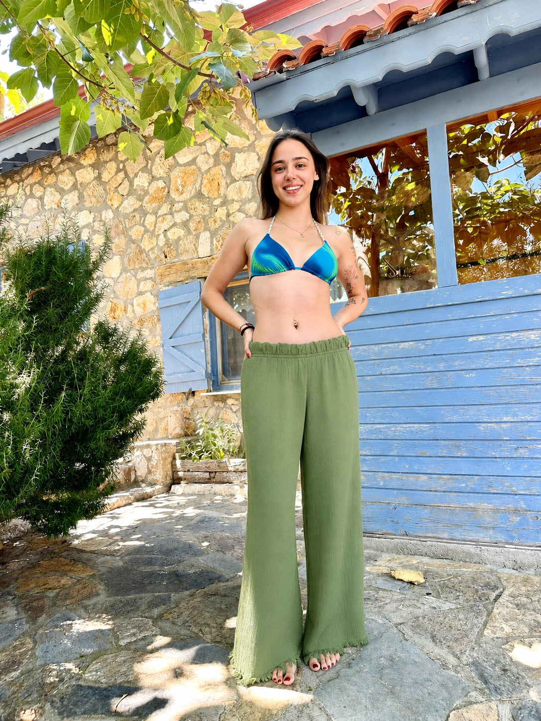 A woman stands outdoors in front of a stone wall and blue wooden door, wearing Nara kimono pant. 