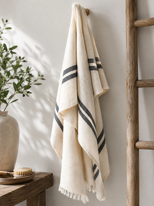 Celine 100% cotton Turkish towel hanging in a neutral bathroom, featuring a natural ivory weave, black stripes and fringed edges.