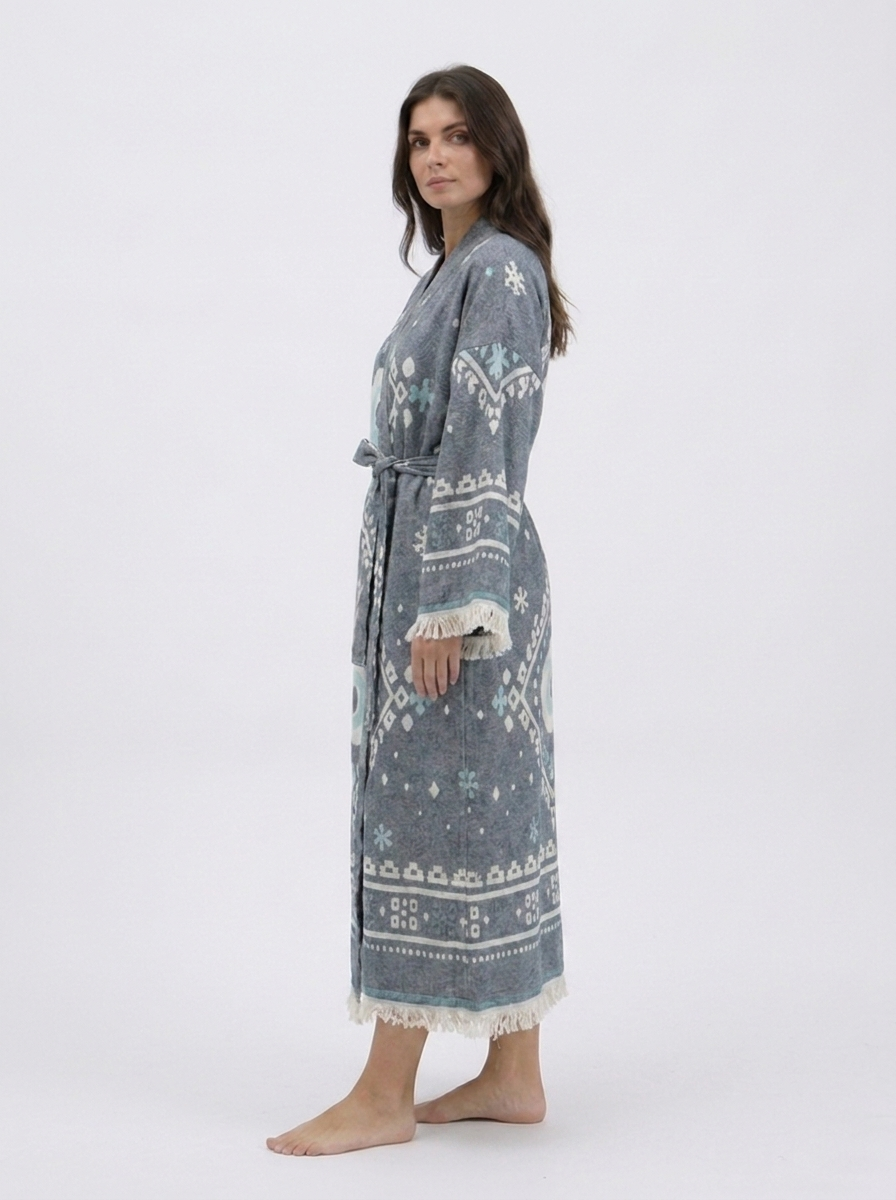 Side view of a long charcoal grey cotton kimono robe showing its relaxed fit, oversized evil eye design, wide patterned sleeves, matching belt, and soft cream fringe along the cuffs and hem.