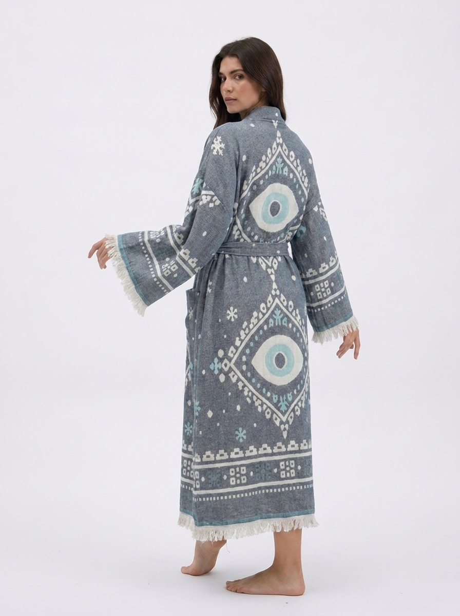 Back view of a charcoal grey cotton kimono robe featuring large white and aqua evil eye designs, geometric motifs, a matching tie belt, wide fringed sleeves, and a relaxed ankle-length silhouette.