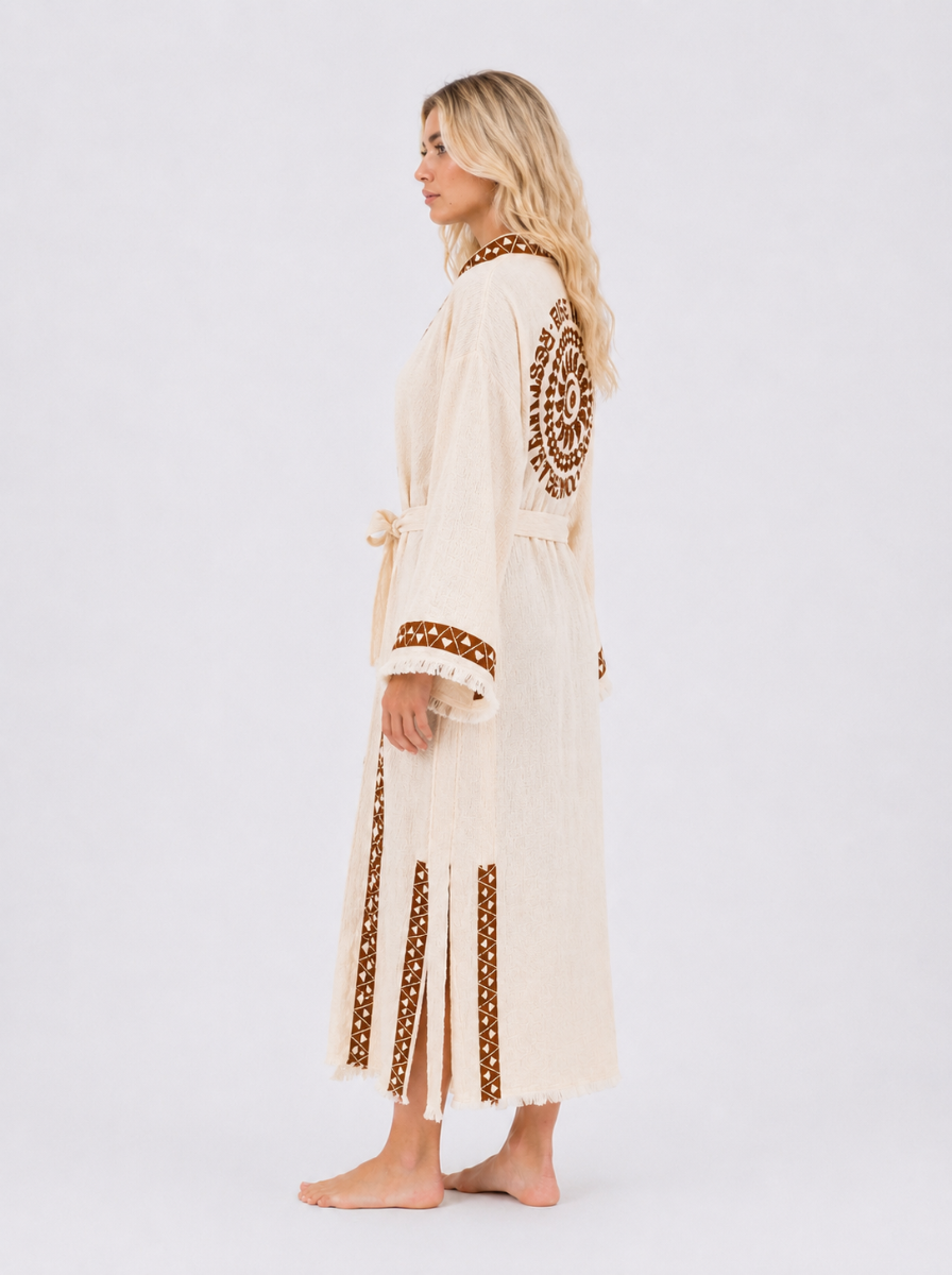 Side view of a cream cotton kimono robe showing the relaxed long fit, brown geometric trim, side slits, matching waist belt, wide fringed sleeves, and celestial back artwork.
