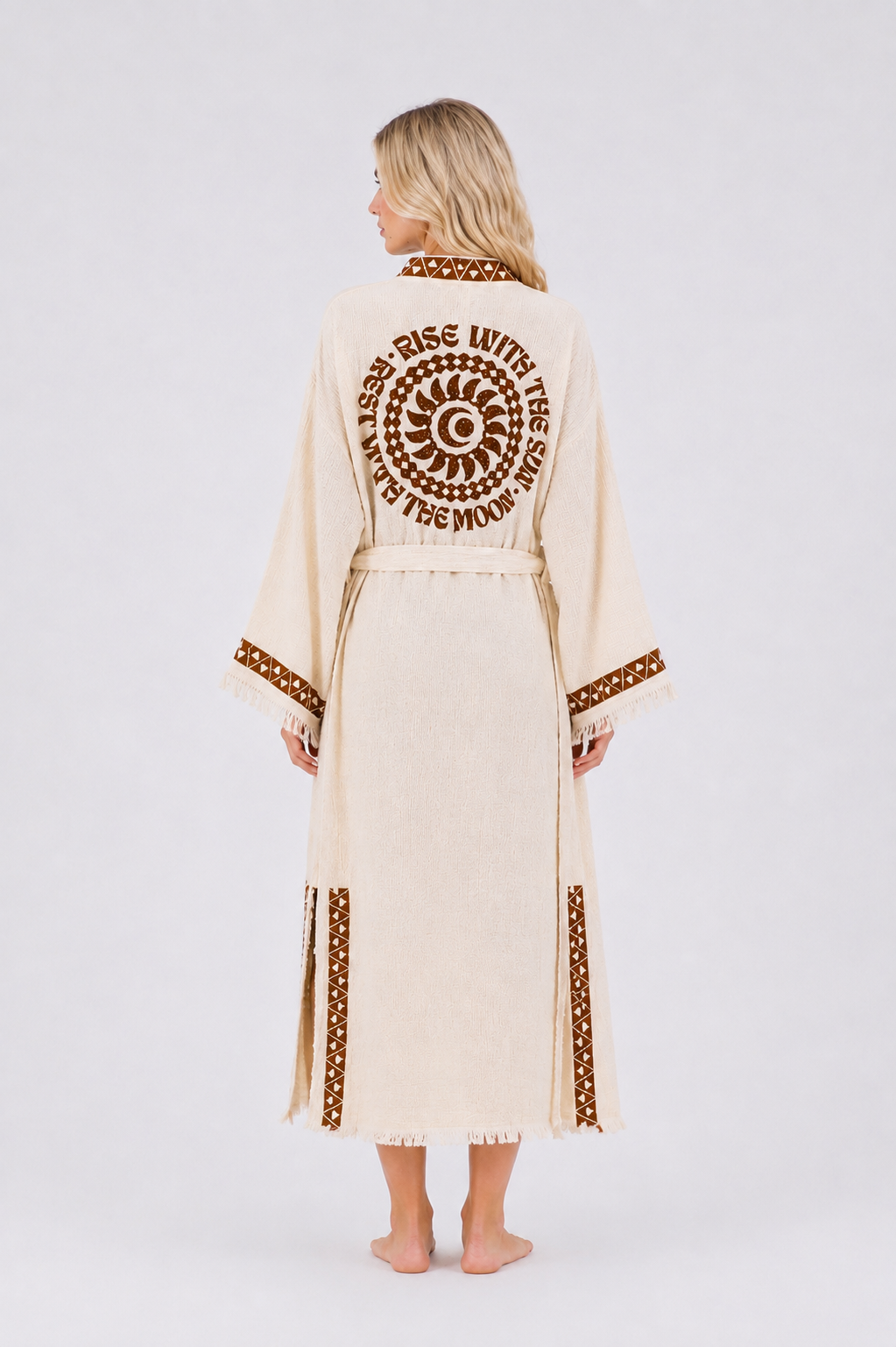 Full back view of a cream cotton kimono robe featuring a brown celestial sun and crescent moon motif with Rise with the Sun, Rest with the Moon lettering, geometric trim, belt, and fringe hem.