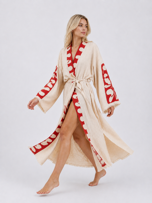 Model walking in a long cream cotton kimono robe with vivid red abstract panels, showing the flowing fabric, wide sleeves, matching waist belt, front opening, and relaxed movement.