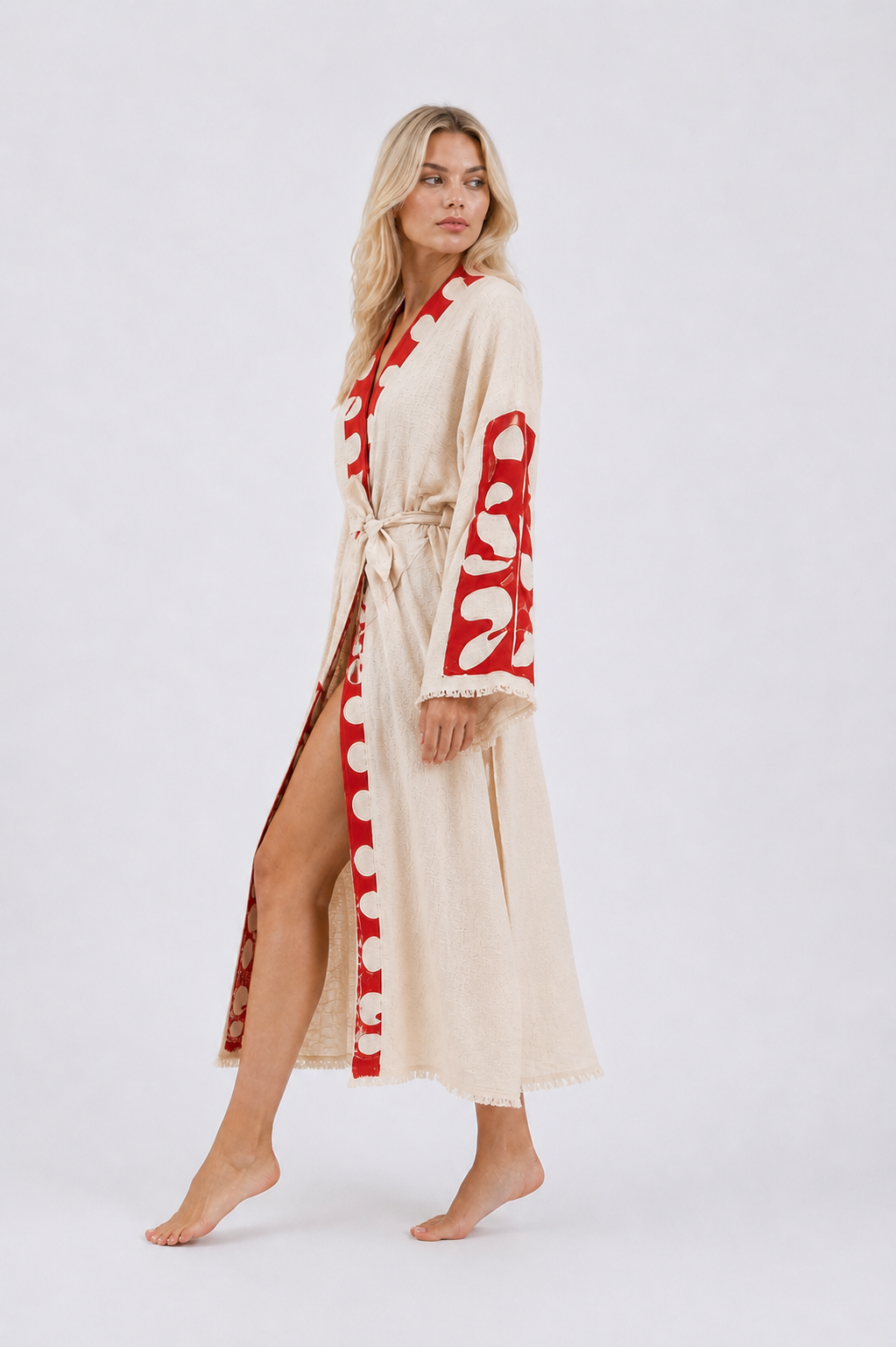 Side view of a model wearing a cream cotton kimono robe with bold red abstract sleeve and neckline panels, a belted waist, side opening, wide sleeves, and ankle-length hem.