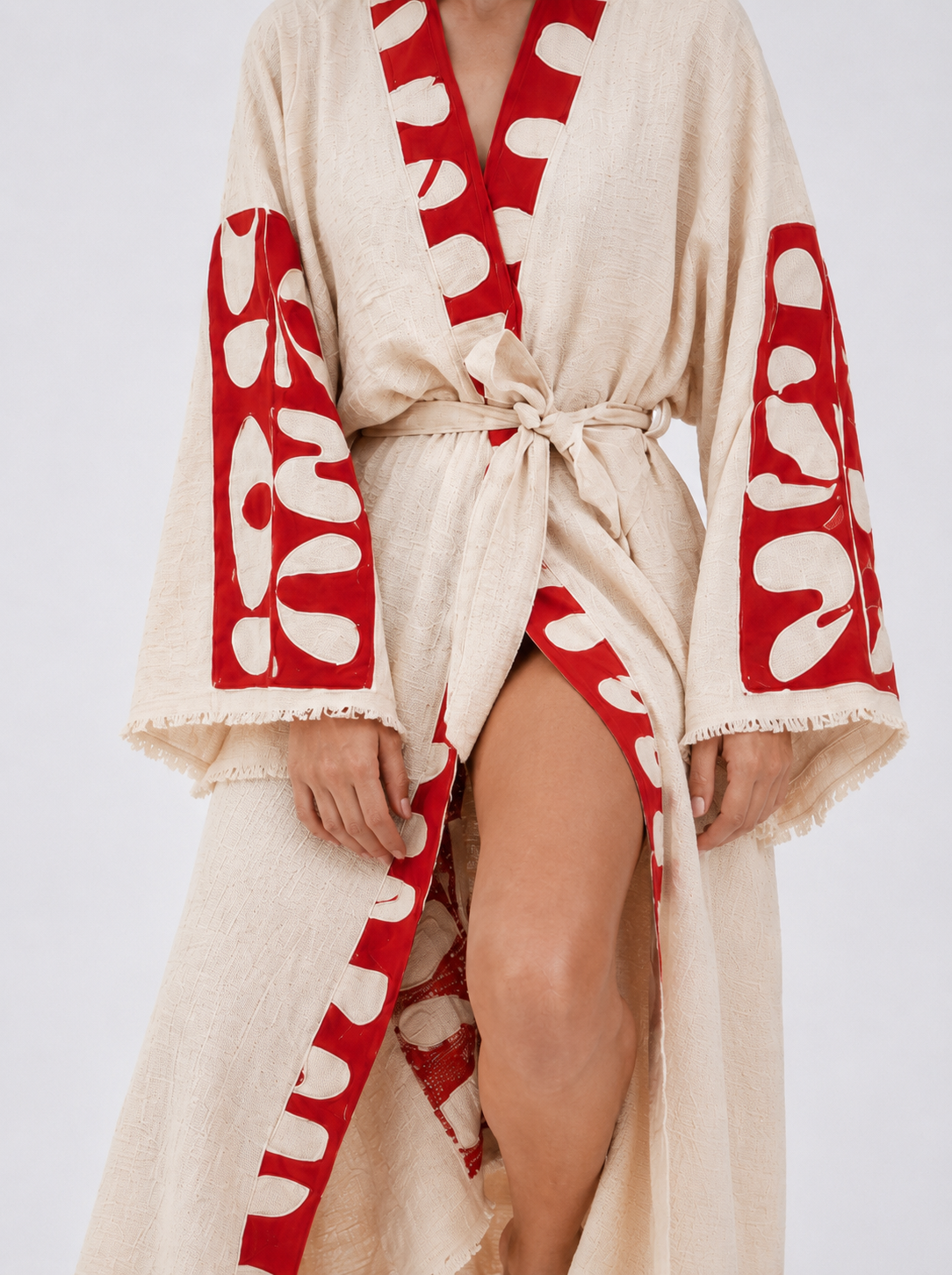 Close-up of a cream textured cotton kimono robe showing the bold red abstract neckline and sleeve panels, matching waist tie, wide sleeves, and delicate fringe edging.