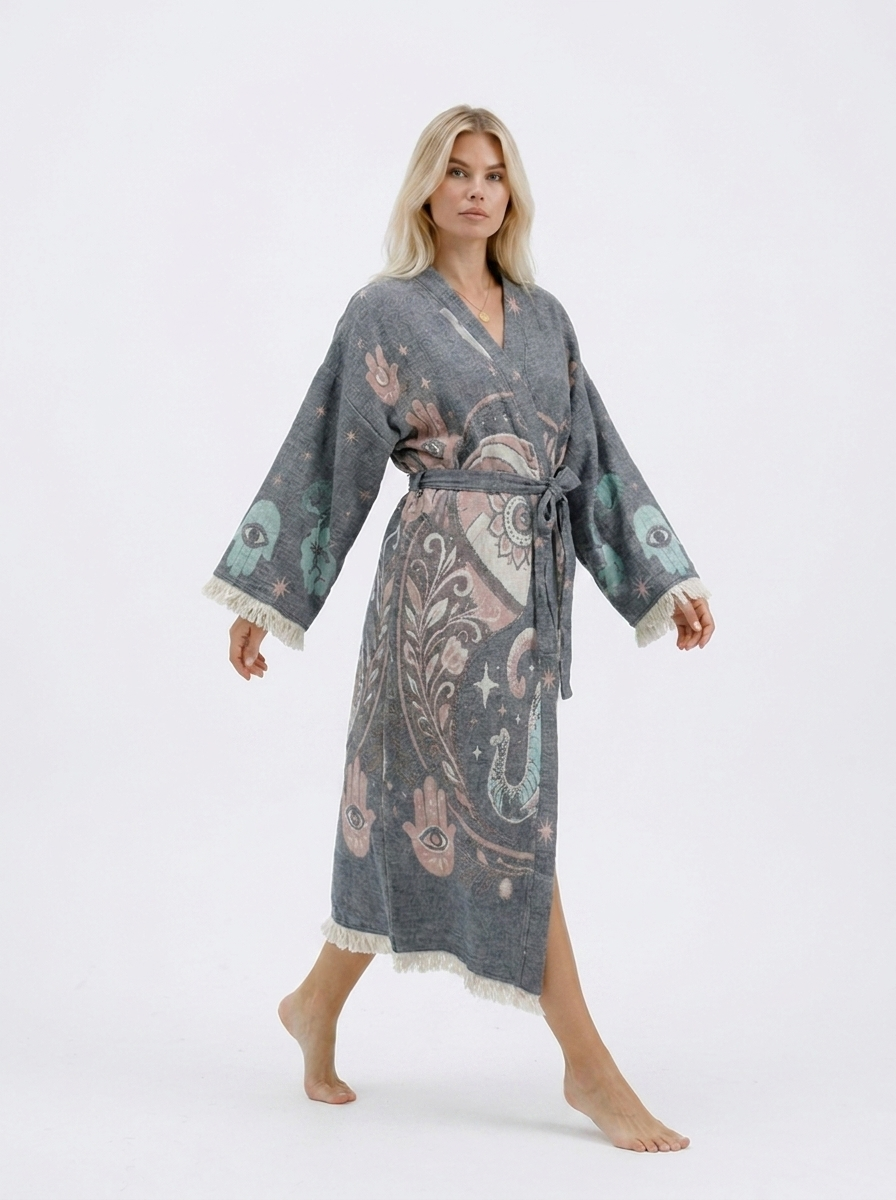 Model walking in a long grey jacquard cotton kimono robe with pastel elephant and Hamsa motifs, showing the flowing silhouette, side opening, wide fringed sleeves, and belted waist.