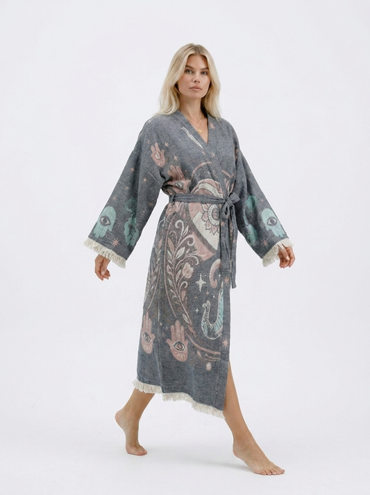 Model walking in a long grey jacquard cotton kimono robe with pastel elephant and Hamsa motifs, showing the flowing silhouette, side opening, wide fringed sleeves, and belted waist.