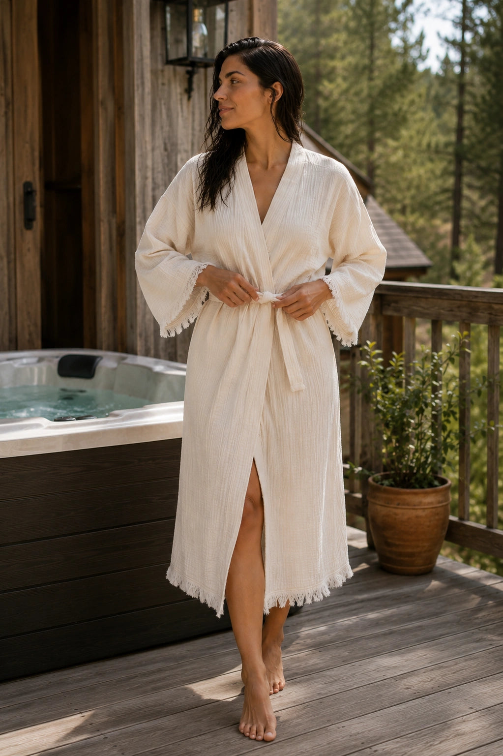 Woman wearing the Happy Horse Muslin Kimono Robe beside an outdoor hot tub, styled as a lightweight spa robe with breathable muslin fabric and fringed hems.
