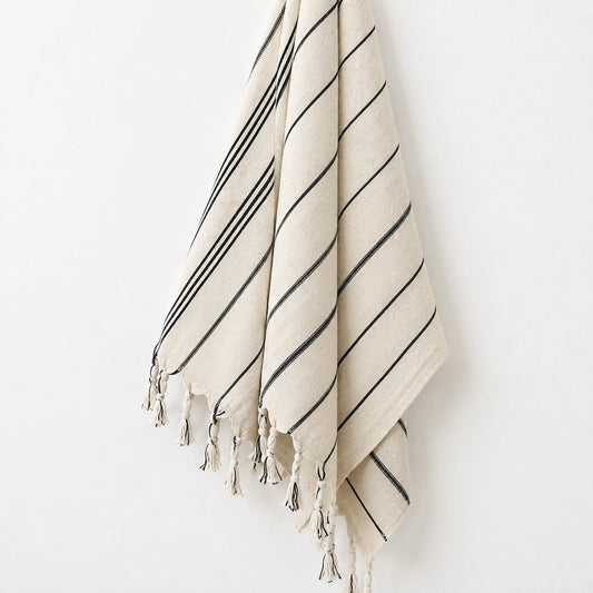 Close-up of Lale Turkish towel showing its natural ivory woven texture, fine black stripes and hand-knotted tassels.