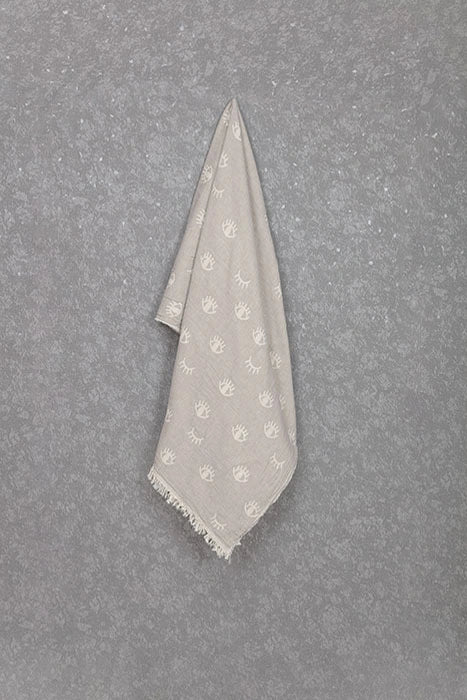 Lia grey cotton Turkish peshtemal towel hanging against a textured wall, showing its eye pattern and soft fringe.