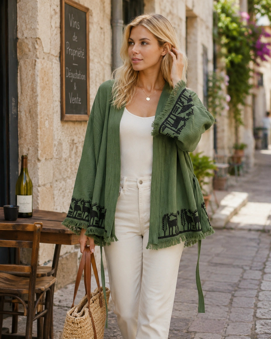 Woman styling the Nara sage green kimono open over a white top and cream pants for casual everyday wear, showing black patterned trim and fringe details.