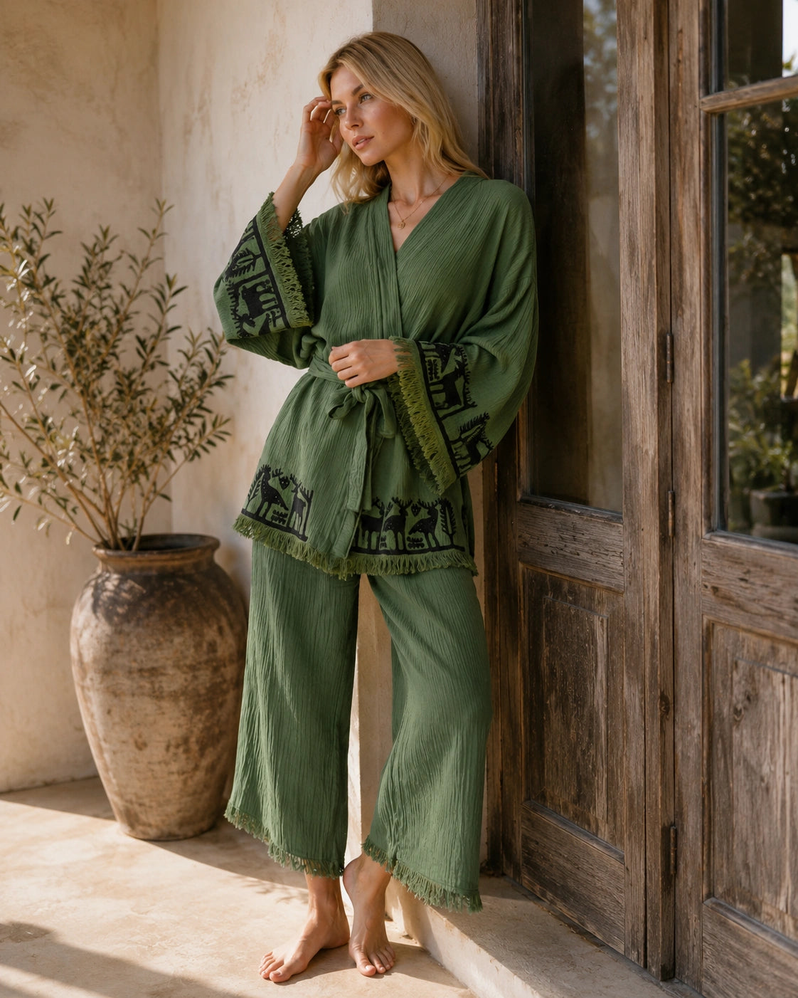 Woman wearing the Nara sage green kimono and wide-leg pants set at home, featuring black artisan-inspired animal motifs, fringed edges and a relaxed belted fit.