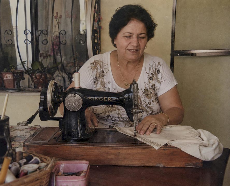 Artisan seamstress sewing cream fabric with gold trim on a vintage Singer sewing machine — Indijio craftsmanship