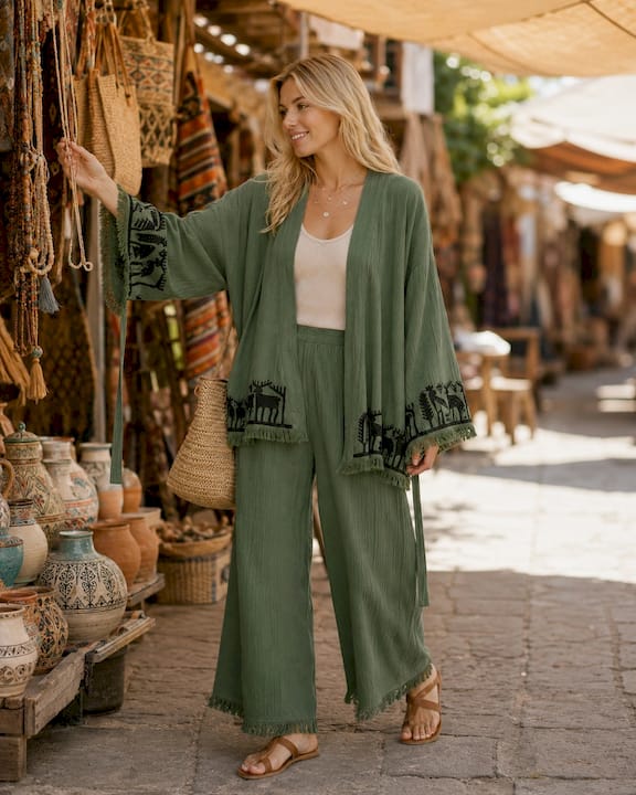 Woman wearing the Nara sage green kimono with matching wide-leg pants while browsing an artisan market, styled open with a neutral top and woven bag.