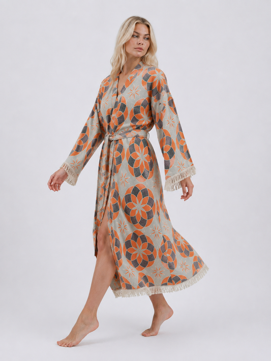 Model walking in a long orange and grey jacquard cotton kimono robe, showing the flowing silhouette, side opening, geometric pattern, belt, and fringe hem.