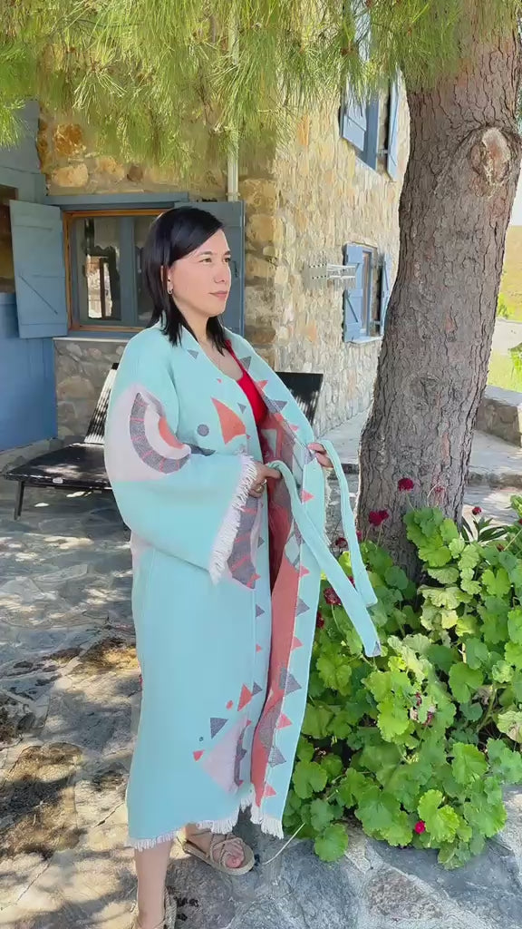 Load video: A woman wearing a Liam kimono robe on a natural stone-wall porch.