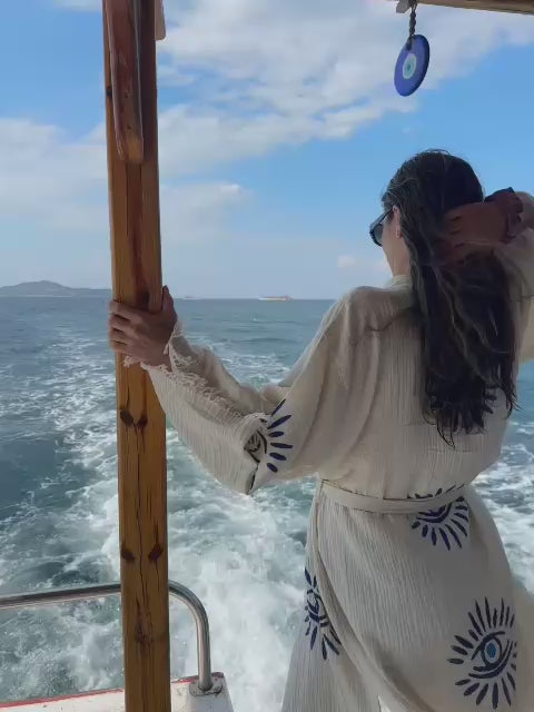 Load video: Woman wearing the Nazar cotton-linen kimono robe by the sea, showing blue evil eye motifs, relaxed fit and breezy resort styling.