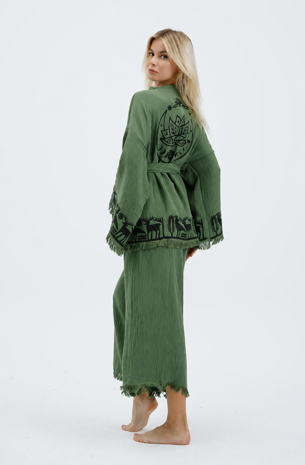Back view of a sage green cotton kimono and wide-leg pants set featuring a large black lotus motif, Anatolian-inspired animal and tree border designs, a matching belt, and fringed edges.